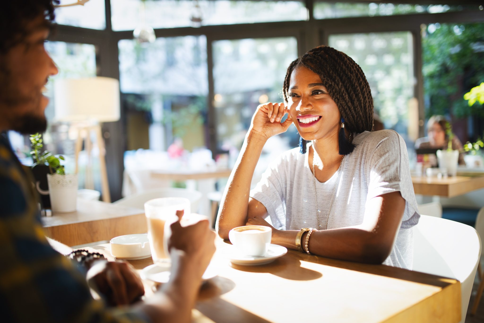 smiling young african couple sitting at a table at a cafe drinking coffee and talking together