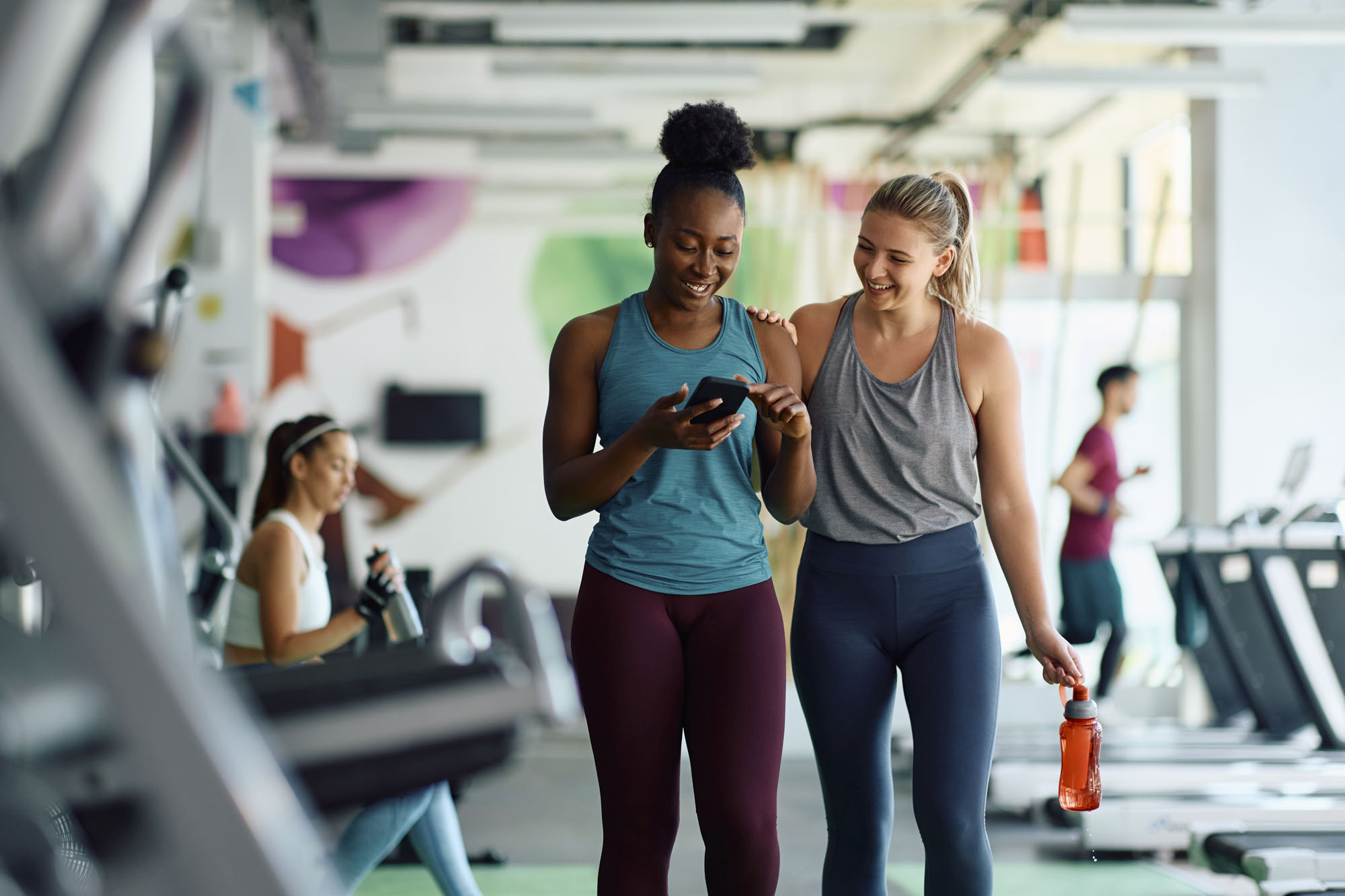 happy athletic women using cell phone during sports training in gym.
