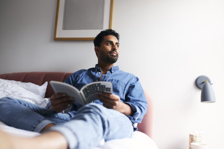 young man relaxing on bed at home enjoying reading book
